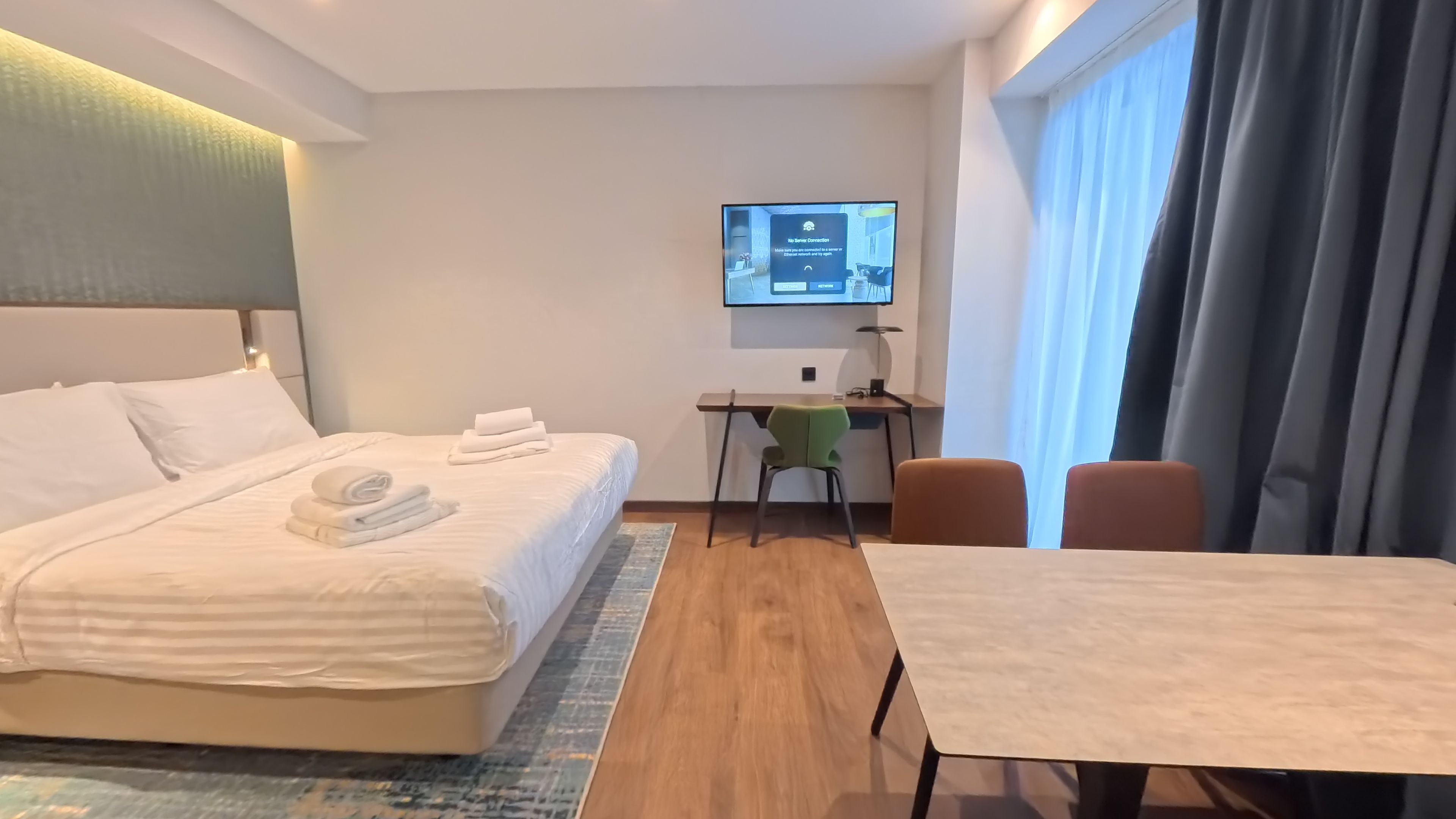 A hotel room with a bed, a desk, a chair, a TV, and a table.