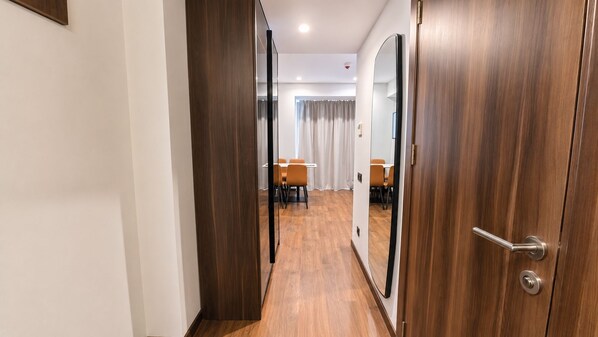 Habitación de hotel con piso de madera, una puerta con manija y vista a un comedor con mesas y sillas.