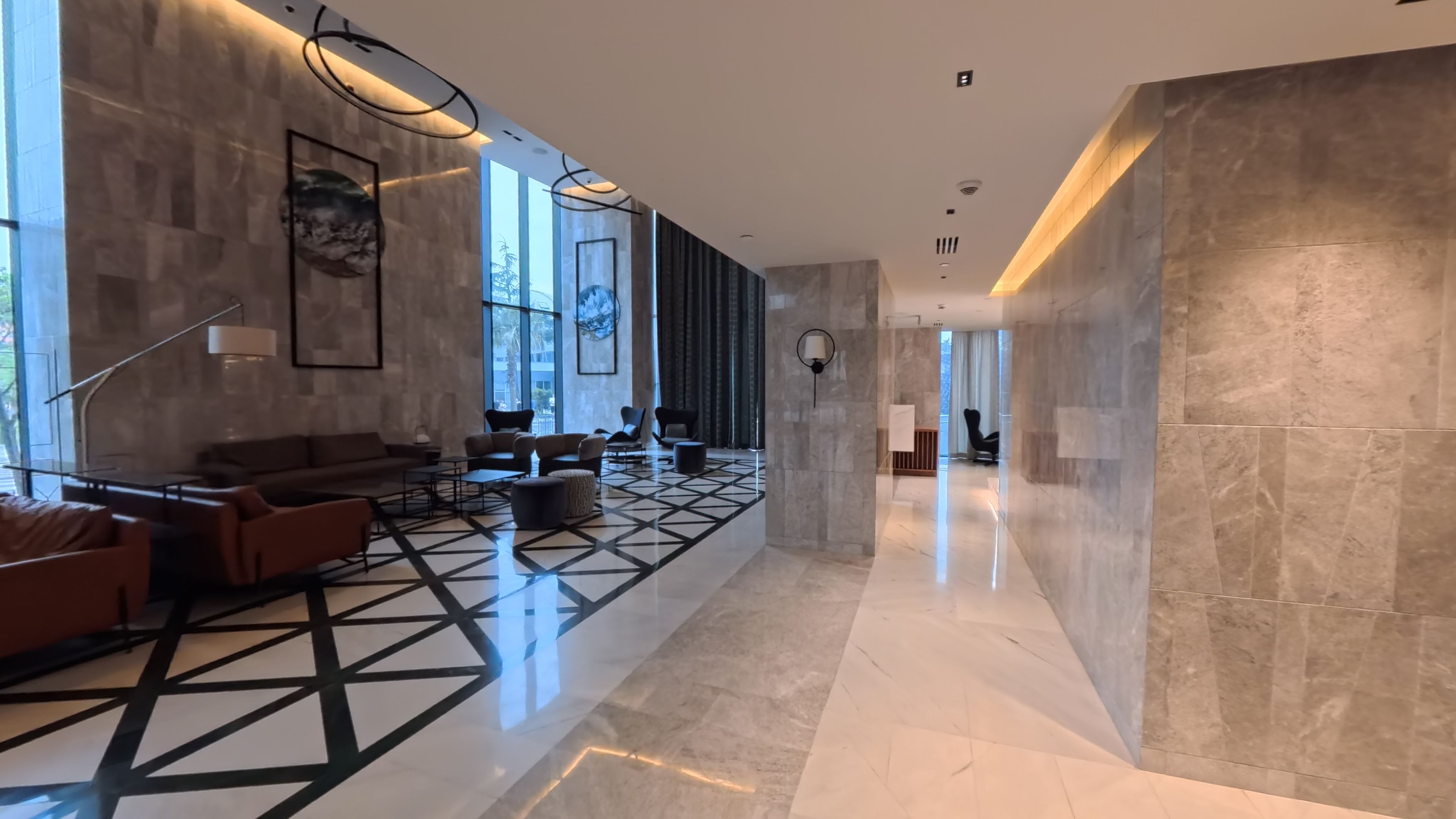 Un hall d’hôtel moderne avec un motif géométrique sur le sol, un espace salon et de grandes fenêtres.