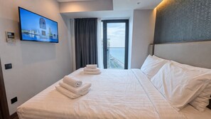 Una habitació d'hotel amb un llit, un televisor de pantalla plana fixat a la paret, una finestra amb cortines i vista a la ciutat.