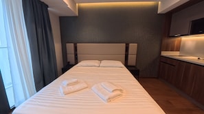 Una habitación de hotel con una cama grande, una mesita de noche, un televisor integrado y un armario de madera.