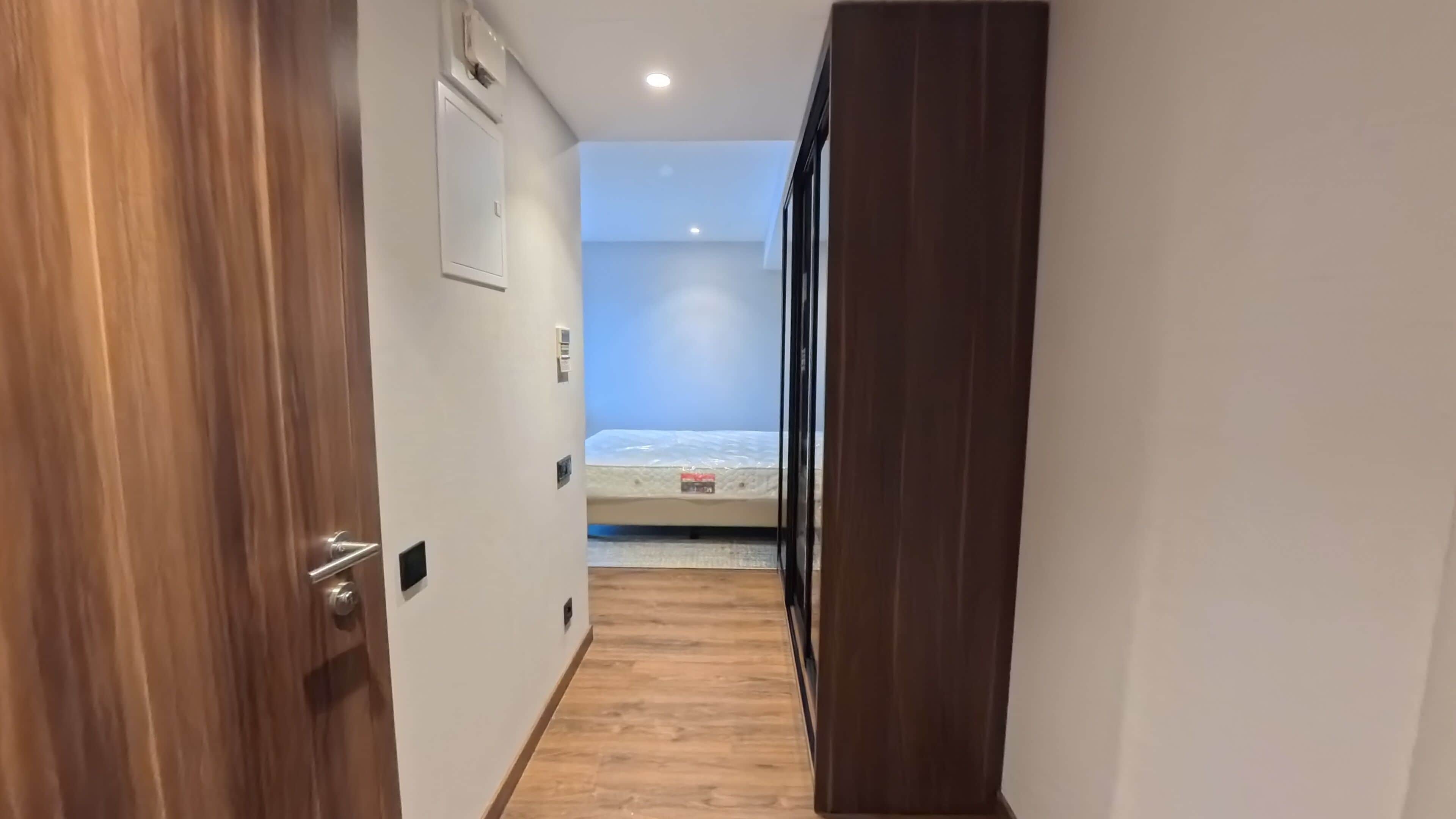 A narrow hallway leading to a bedroom with a bed and a window.