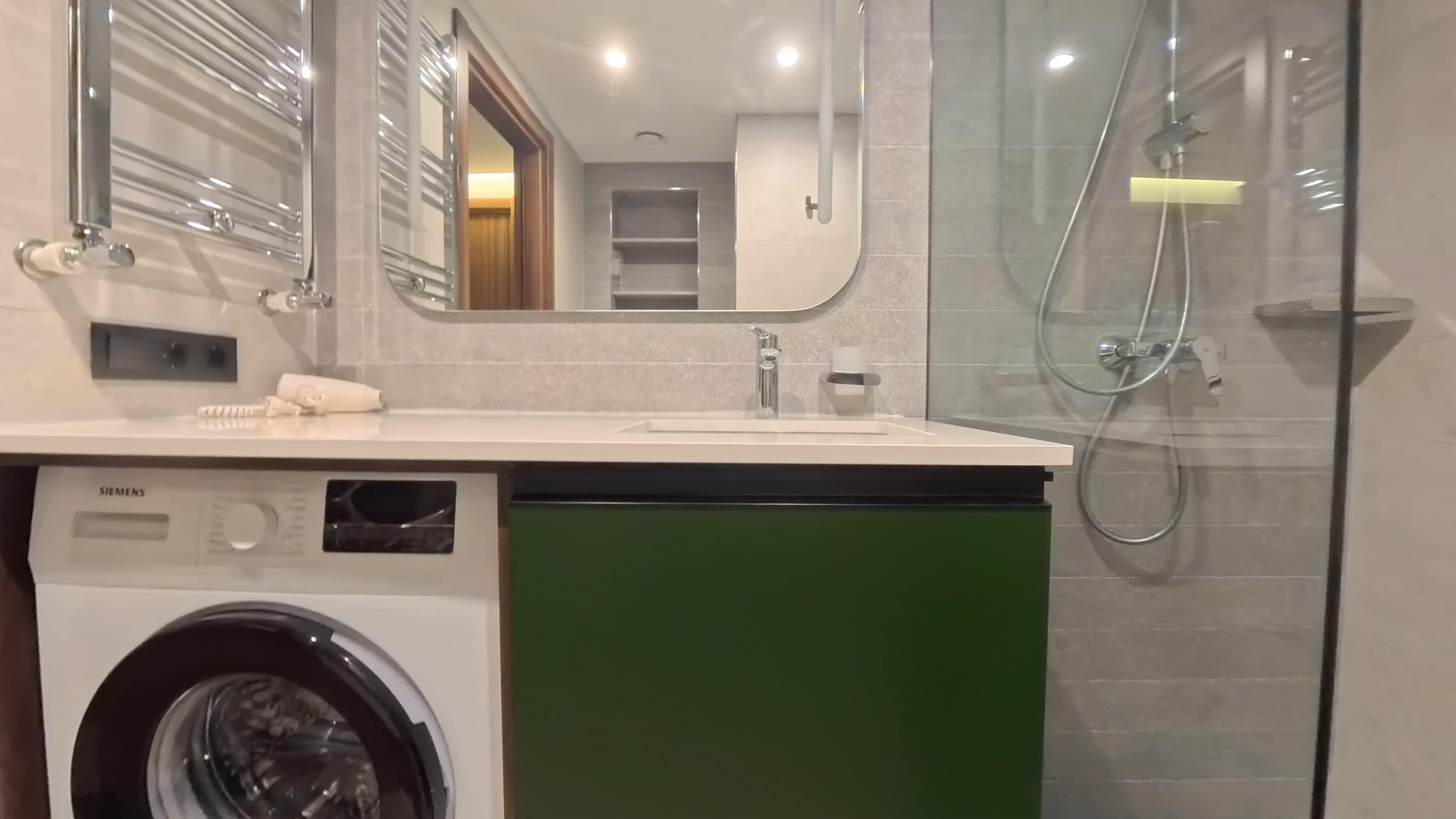A modern bathroom with a washing machine, a sink, and a shower.