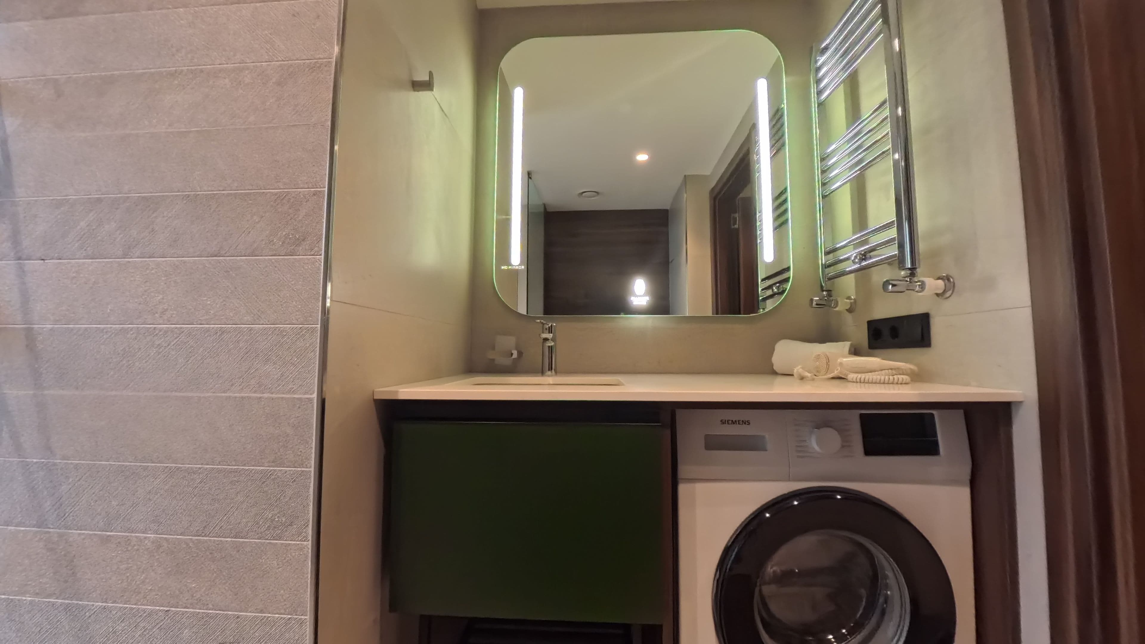 A hotel bathroom with a sink, mirror, towel, and a washing machine.