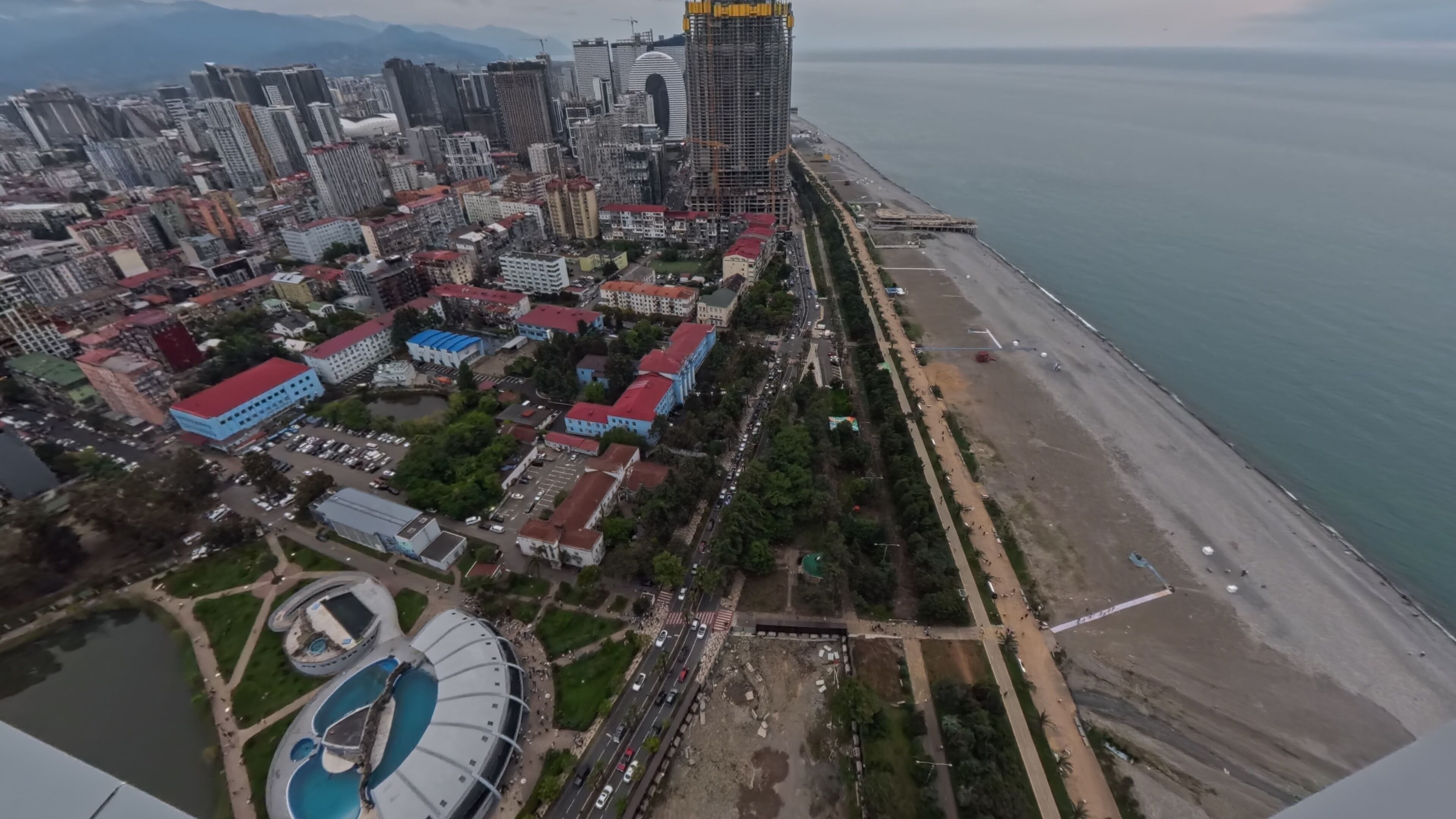 An aerial view of a coastal city with high-rise buildings, a beach, and a large swimming pool complex.