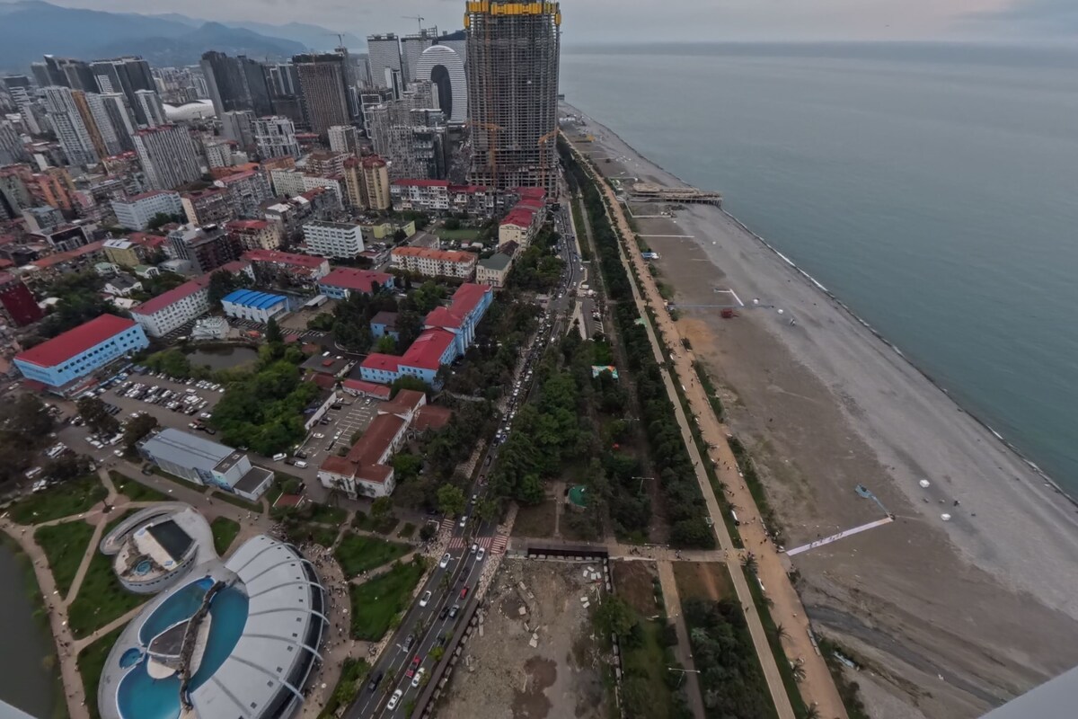 An aerial view of a coastal city with high-rise buildings, a beach, and a large swimming pool complex.