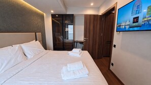 Habitación de hotel con una cama grande, un televisor en la pared y vistas a un paisaje urbano.