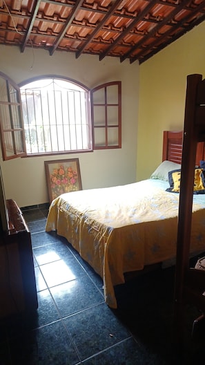 A bedroom with a bed, a window with bars, a painting, and a tiled floor. - House in Saquarema, spacious with games room and gourmet area!!! (Saquarema)