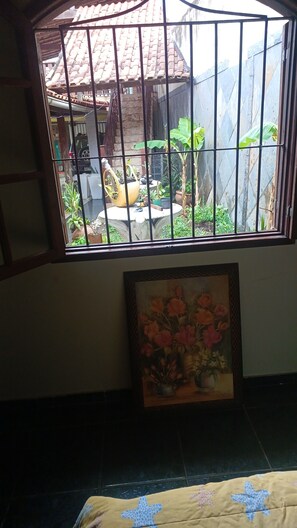 A room with a window overlooking a courtyard, a framed painting of flowers, and a bed with a patterned cover. - House in Saquarema, spacious with games room and gourmet area!!! (Saquarema)