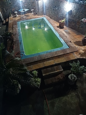 A rectangular pool with a stone border, surrounded by potted plants and a stone wall. - House in Saquarema, spacious with games room and gourmet area!!! (Saquarema)