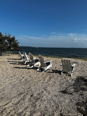 Ein Strand mit mehreren Adirondack-Stühlen, die zum Meer hin ausgerichtet sind.