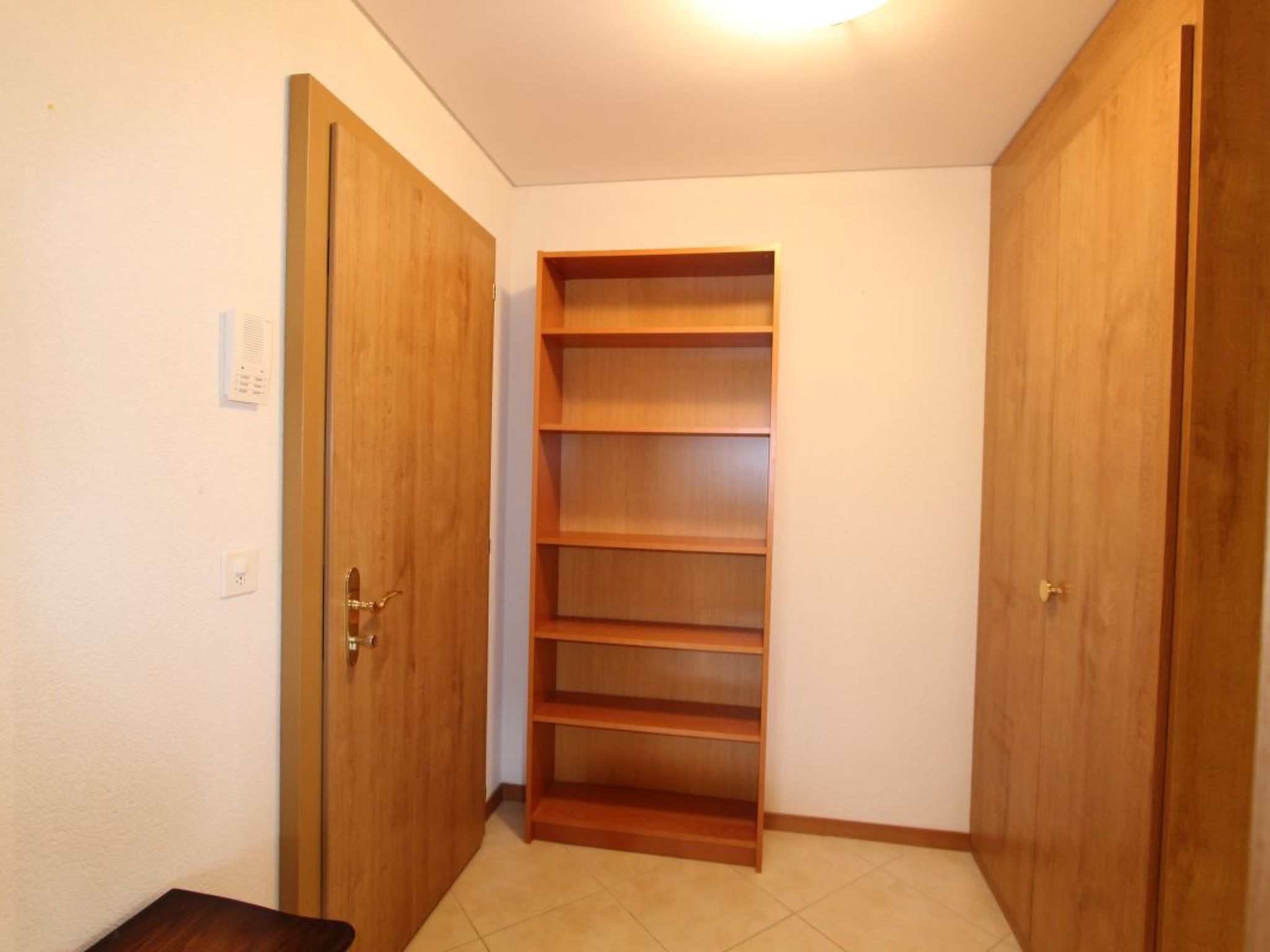Ein Korridor mit einer Holztür links, einem Holzschrank mit mehreren Einlegeböden und einer weiteren Holztür rechts.