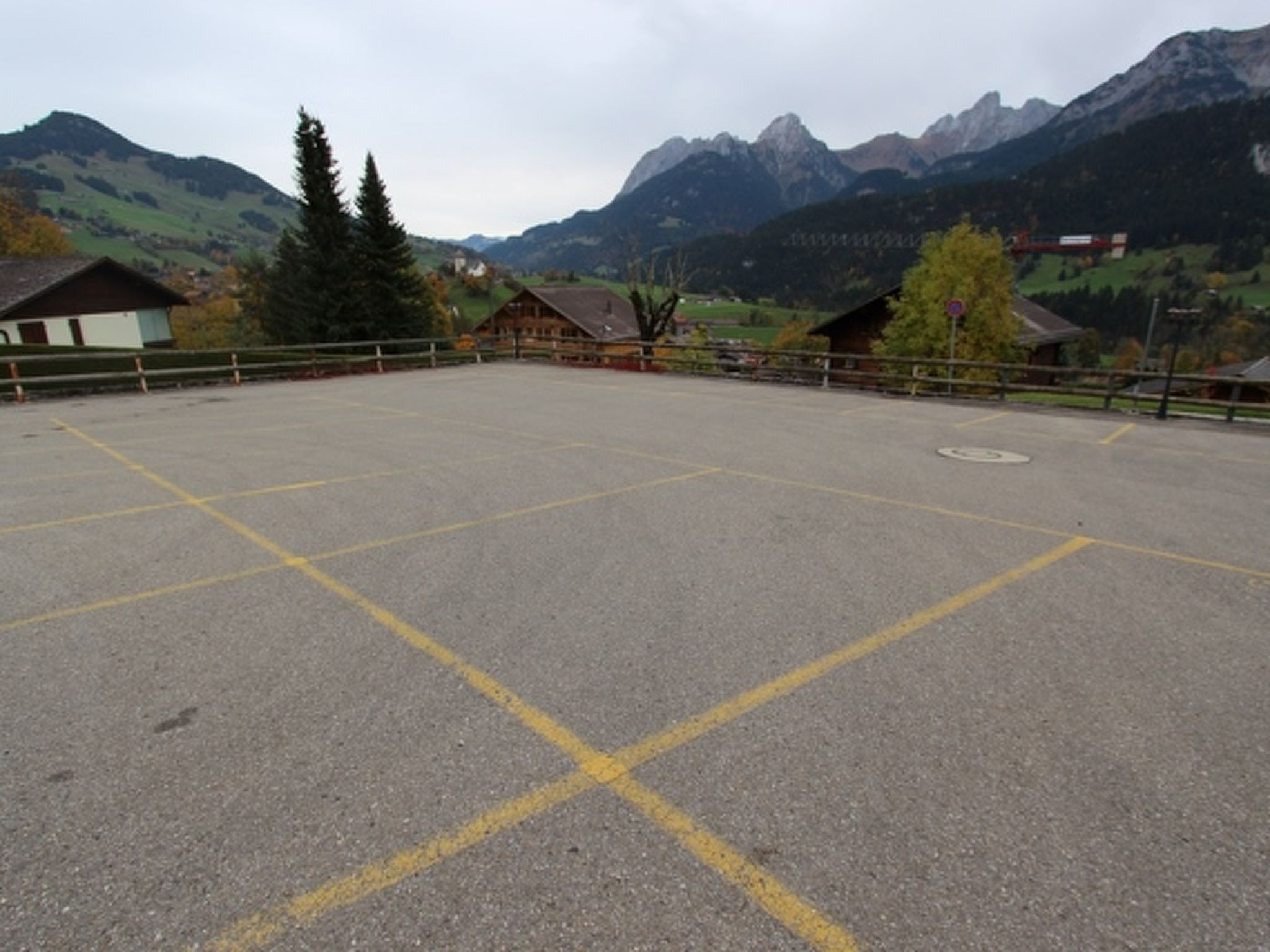 Ein freier Parkbereich mit ausgewiesenen Stellplätzen, umgeben von Gebäuden und Bergen im Hintergrund.