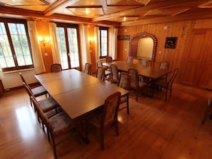 A wooden-paneled dining room with a large table and chairs, windows with curtains, and a brick archway.