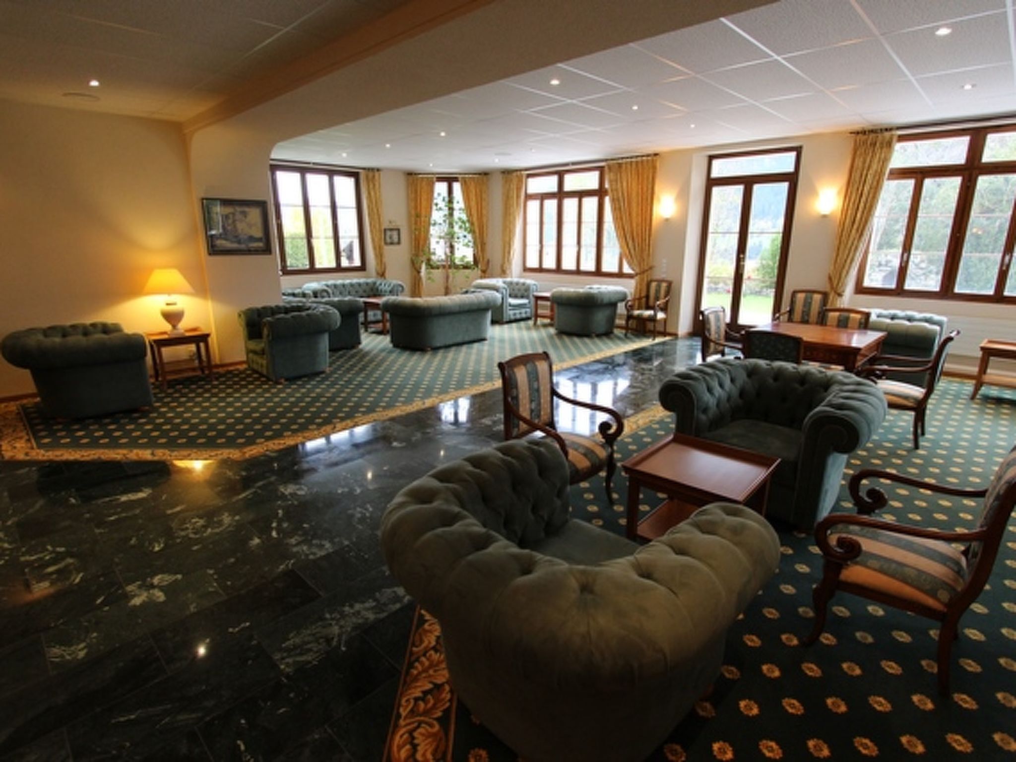 A spacious lobby with multiple seating areas, including sofas and armchairs, arranged around a central coffee table.