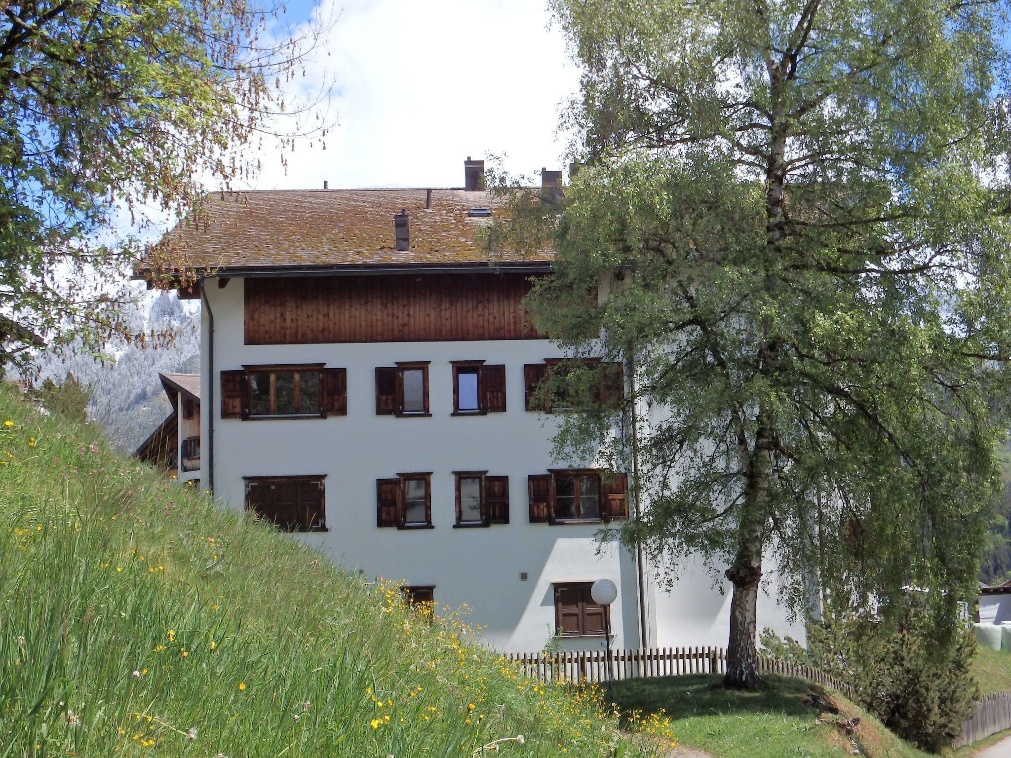 Un immeuble à plusieurs étages, doté d’un toit en pente, de volets en bois et d’une façade blanche.