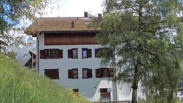 Un immeuble à plusieurs étages, doté d’un toit en pente, de volets en bois et d’une façade blanche.