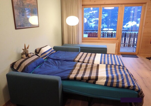 A bedroom with a bed, a sofa, a window with a view of trees, and a lamp. - Carmen's Oase, (Pany), by Interhome (Pany)