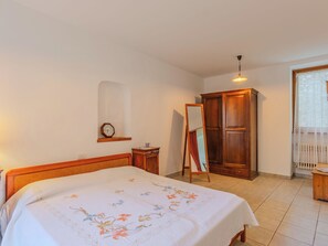 A bedroom with a bed, a wooden wardrobe, a mirror, a clock, and a window with curtains. - La Finestra sul Lago by Interhome (Porlezza)