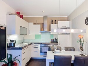 A compact kitchen with white cabinetry, a built-in oven, and a dining area with a table and chairs. - Mountain Resort-Kaprun by Interhome (Kaprun)