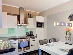 A modern kitchen with built-in appliances, a dining area with a table and chairs, and a wall-mounted clock. - Mountain Resort-Kaprun by Interhome (Kaprun)