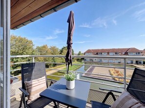 Een balkon met een tafel, stoelen, een plant in pot en een parasol.