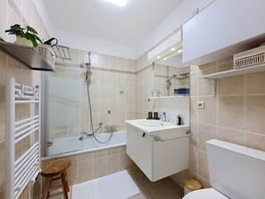 Een moderne badkamer met een glazen douchecabine, een witte wastafel en een toilet.