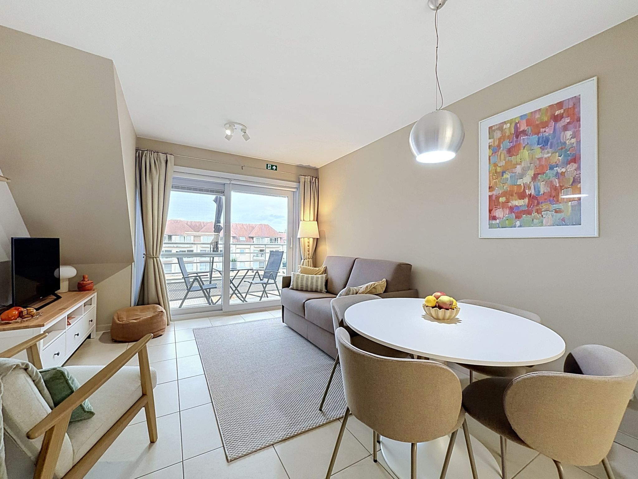 Ein modernes Hotelzimmer mit Balkon, einem Essbereich, einer Couch und einem Fernseher.