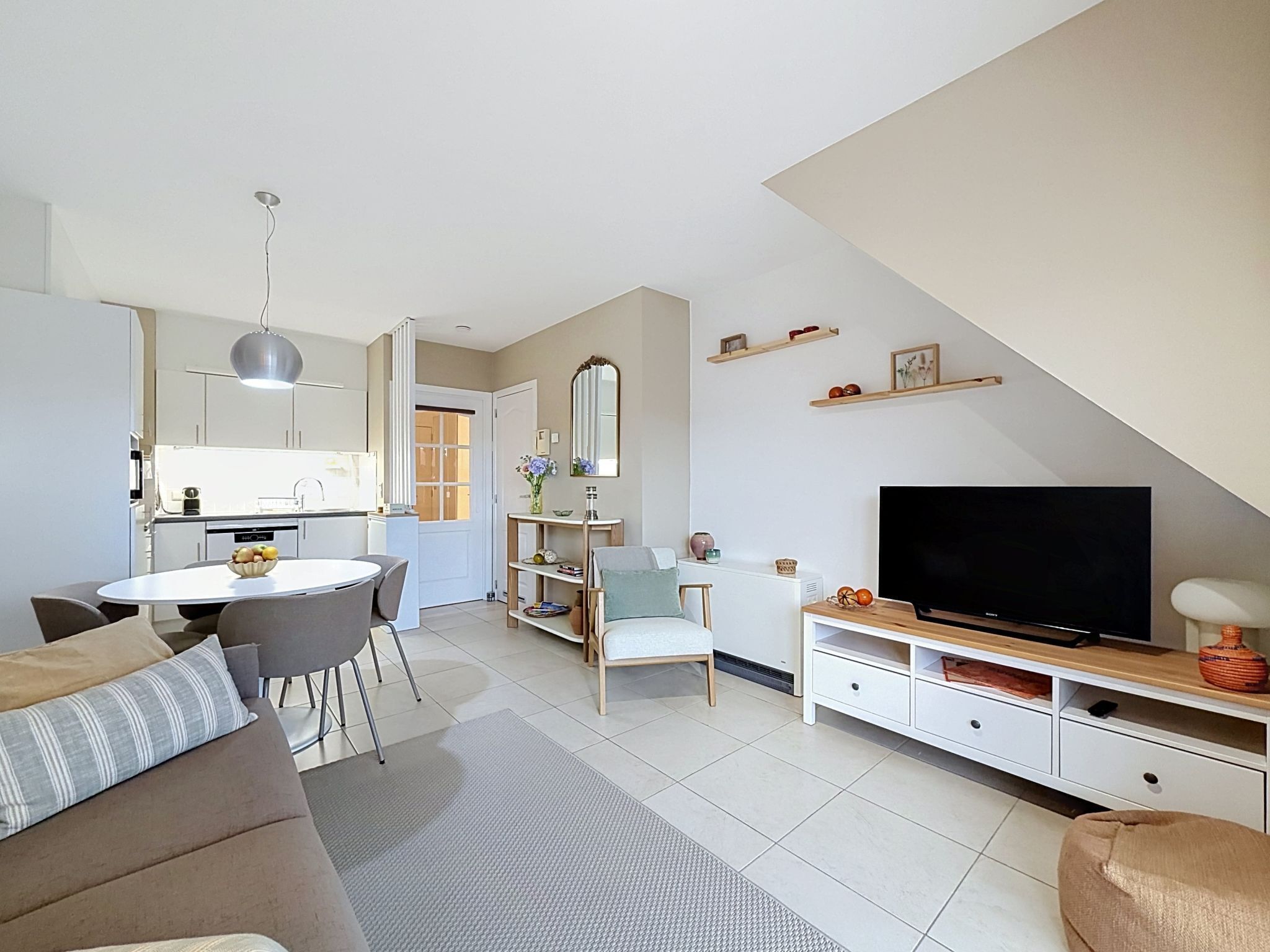 A modern living room with a TV, sofa, dining table, and kitchen area.