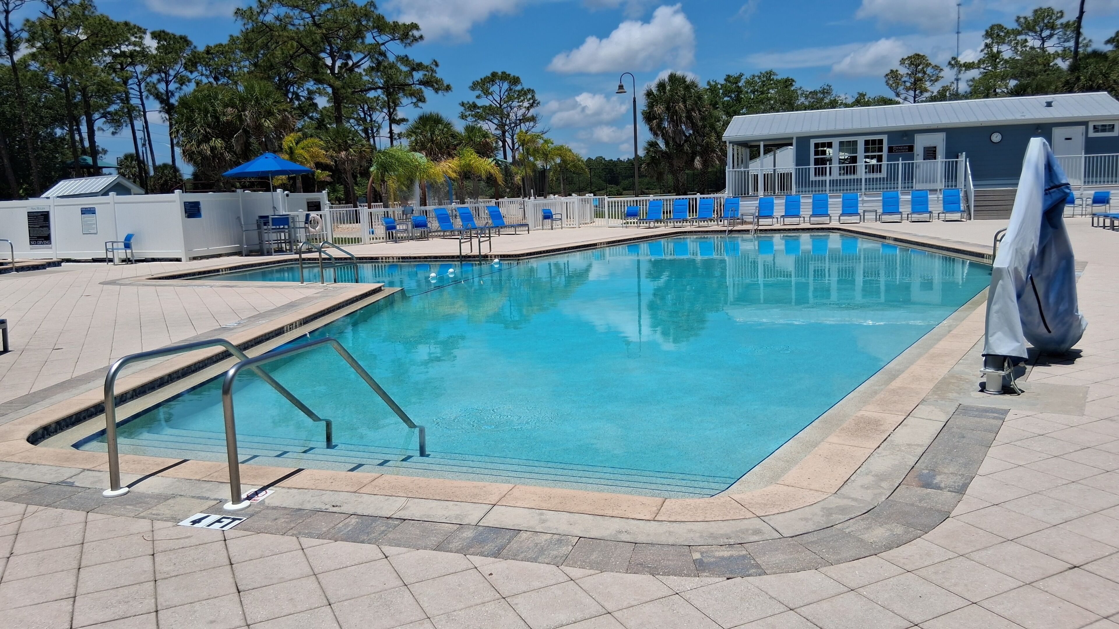 Une piscine avec une terrasse carrelée, des chaises longues bleues et un espace abrité.