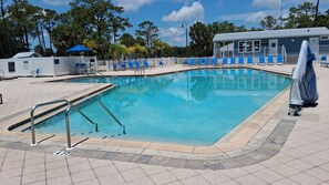 A swimming pool with a tiled deck, blue lounge chairs, and a covered area.