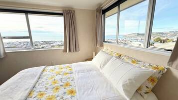 Een slaapkamer met een bed, een raam met gordijnen en uitzicht op een stad.