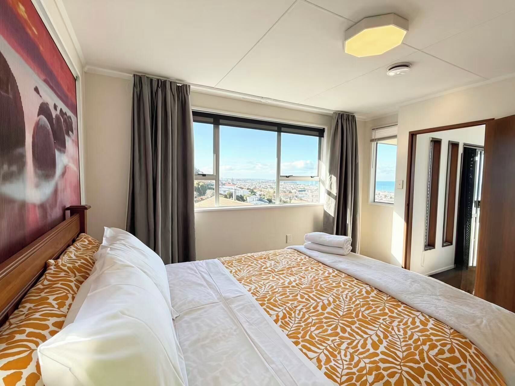 Een hotelkamer met een bed, een groot raam met uitzicht op de stad en een schilderij aan de muur.