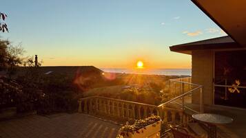 Ein Balkon mit Blick auf den Sonnenuntergang über dem Meer, einer Topfpflanze und einem Tisch mit Stühlen.