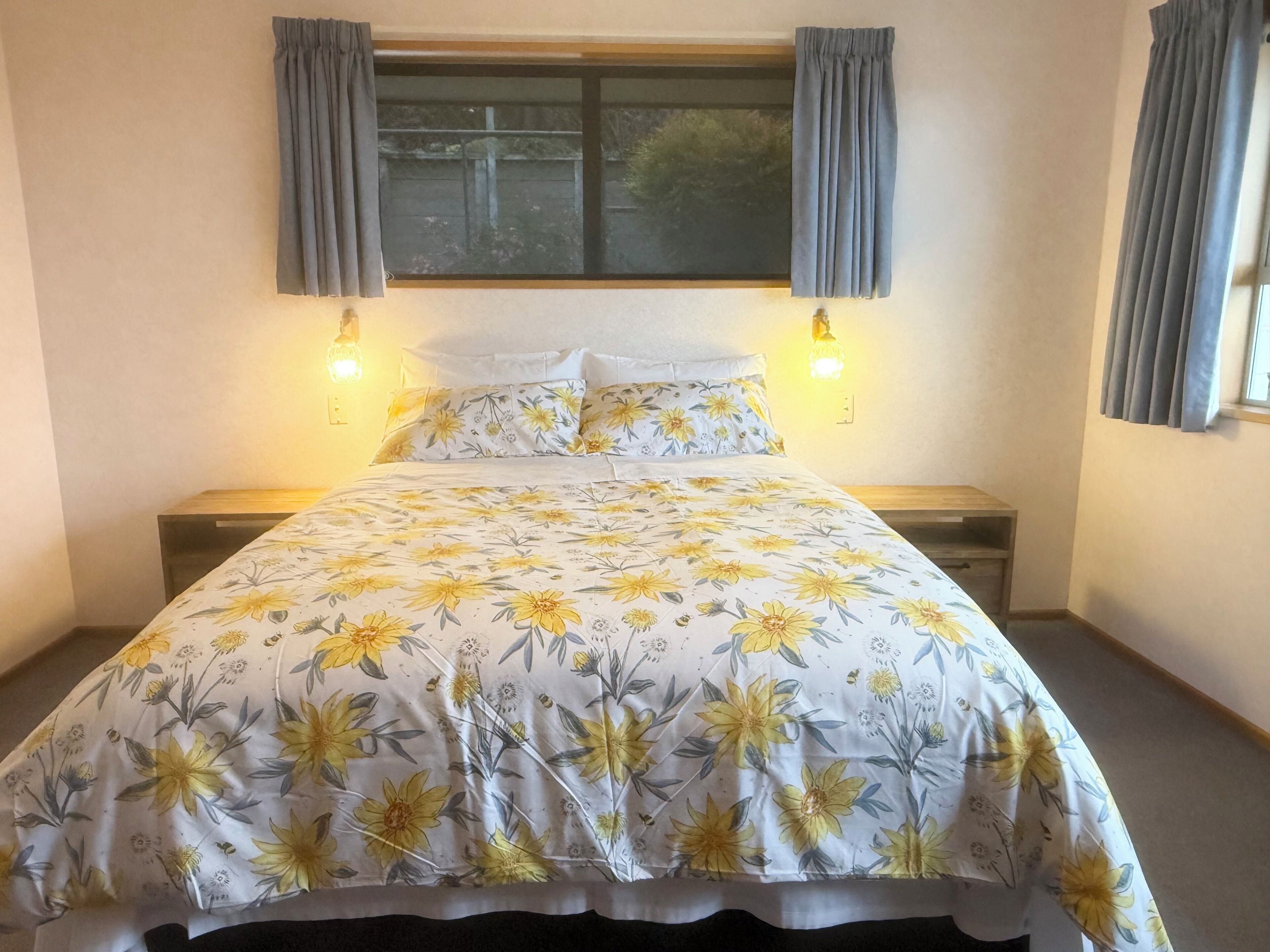A bed with a floral bedspread, two bedside lamps, a window with curtains, and a nightstand.