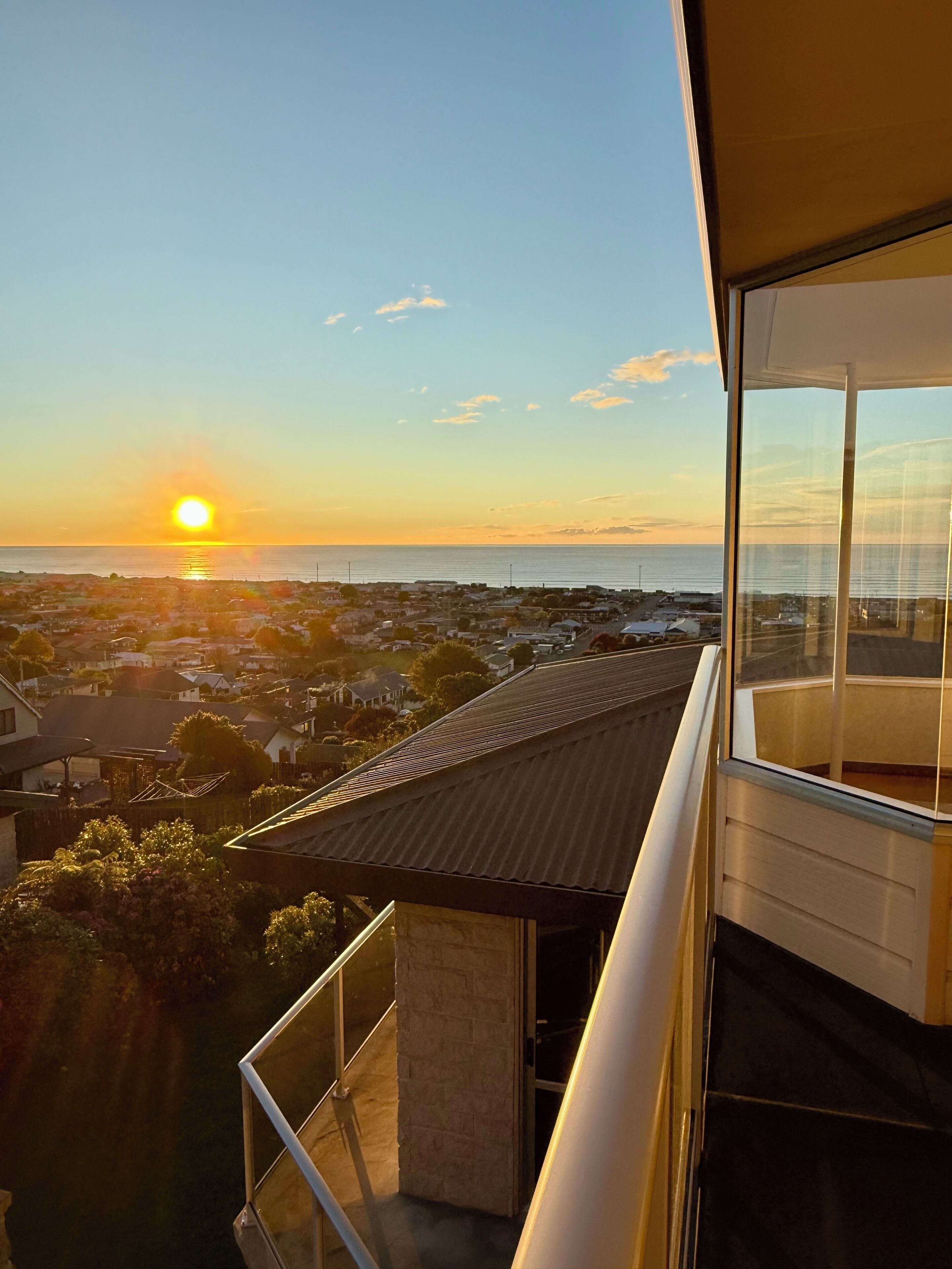 Ein Balkon mit Blick auf ein Wohngebiet und das Meer bei Sonnenuntergang.