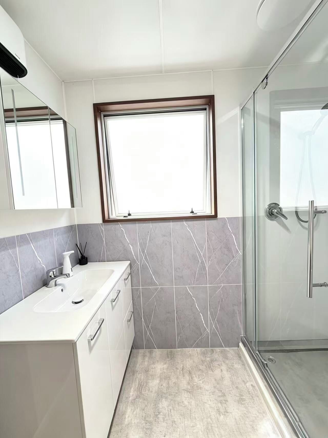 A modern bathroom with a glass shower enclosure, a vanity with a sink, and a window above the mirror.