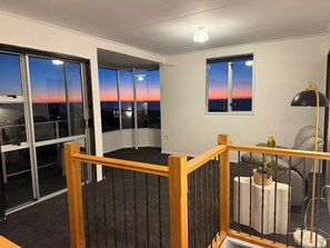 A room with large windows, a staircase, and a view of the sunset.