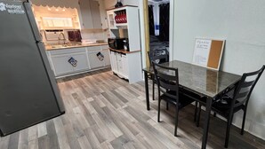 A compact kitchen with a refrigerator, microwave, and cabinets. There is a dining table with chairs.