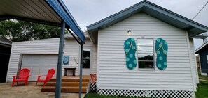 Une maison de plain-pied avec un garage, une véranda et une petite terrasse avec des chaises rouges.