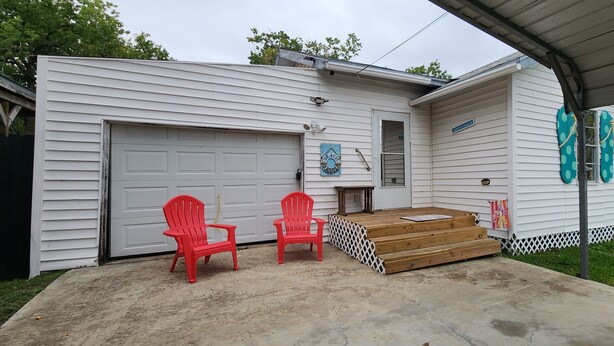 A residential garage with two red plastic chairs, a wooden bench, and a small porch area.