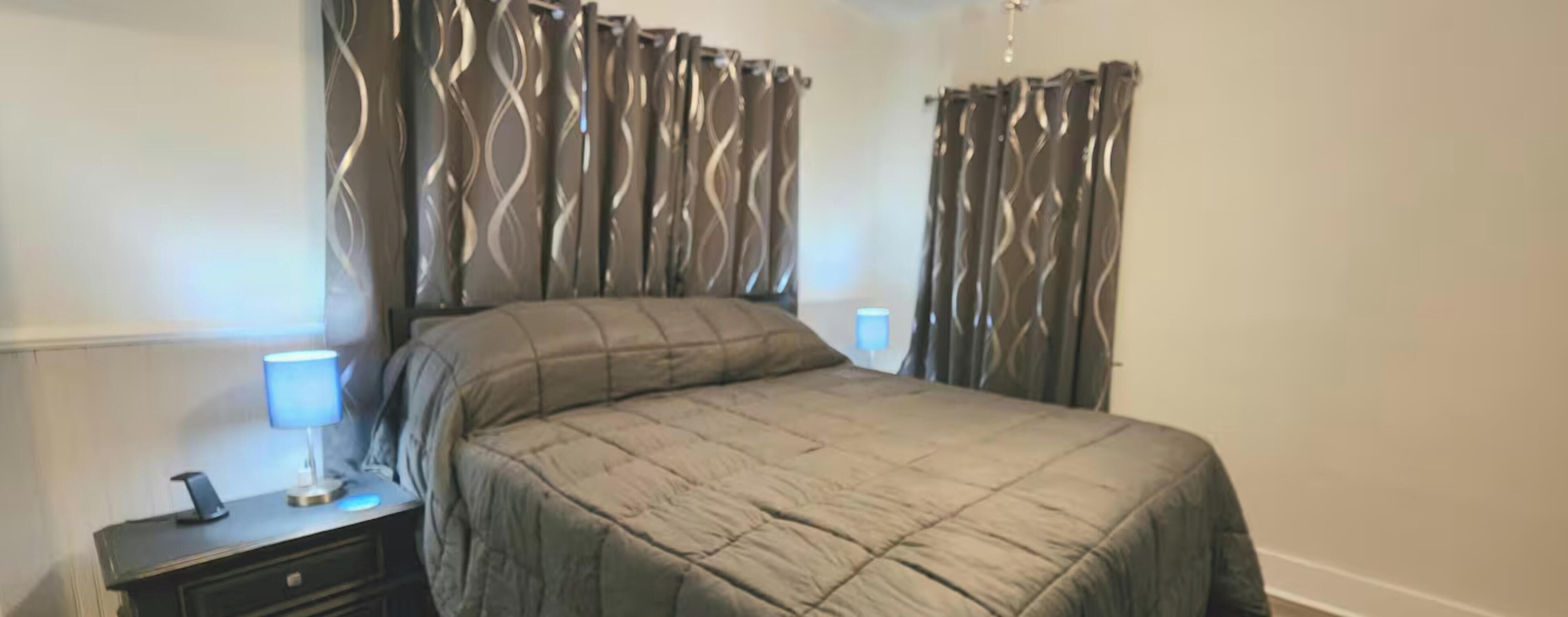 A bedroom with a bed, curtains, a nightstand, and a lamp.
