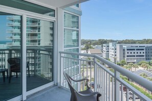 A balcony with a view of a residential area, including a building with multiple balconies and a parking garage. - Amazing Oceanfront View Unit with Pool Access (Myrtle Beach)