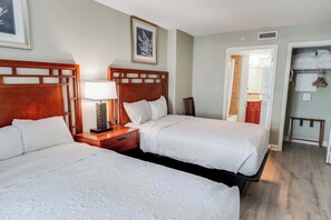 Ein Hotelzimmer mit zwei Betten, einem Nachttisch mit Lampe, einem gerahmten Bild an der Wand und einem durch eine offene Tür einsehbaren Badezimmer.
