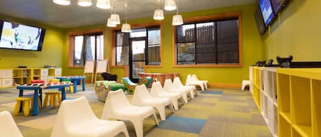 Una sala de jocs infantil amb mobles colorits, una televisió i un gran finestral.