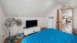 Ein Schlafzimmer mit einem Bett, einem Fernseher, zwei Ventilatoren und einer Kommode.