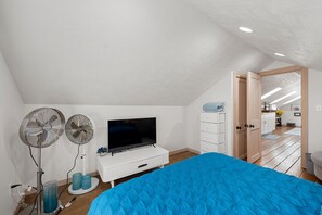 Ein Schlafzimmer mit einem Bett, einem Fernseher, zwei Ventilatoren und einer Kommode.