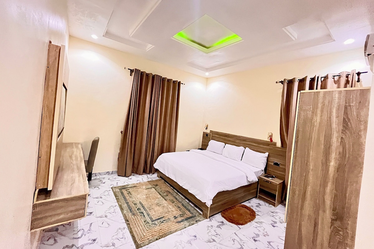 A bedroom with a bed, nightstand, curtains, and a ceiling light fixture.
