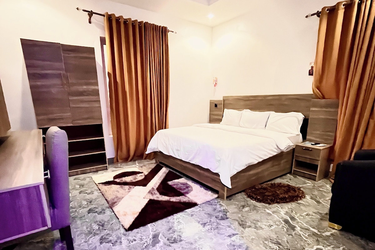 A bedroom with a bed, a nightstand, a chair, and a large rug.