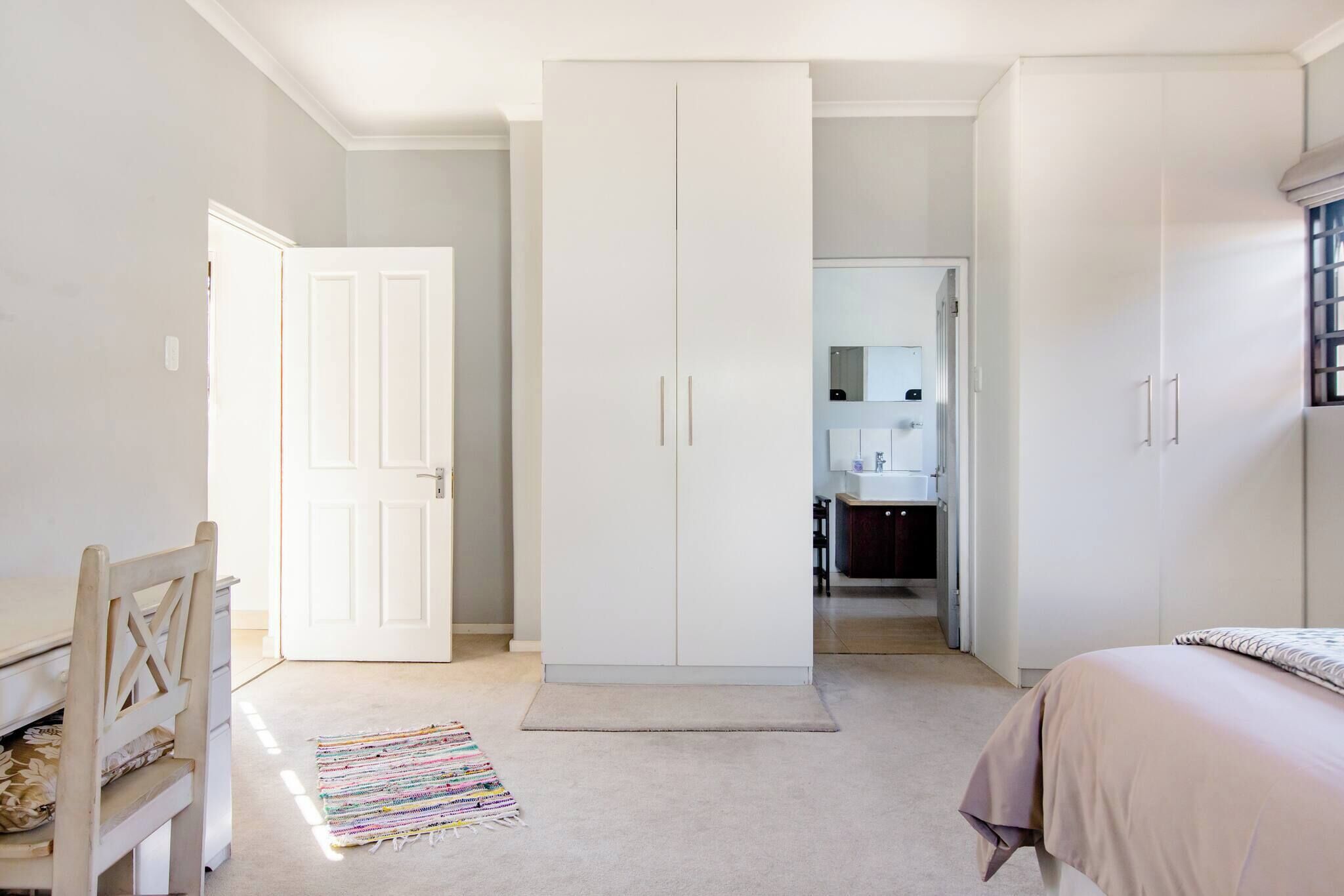 Une chambre à coucher comprenant un lit, un bureau, une armoire et une salle de bain visible à travers une porte ouverte.